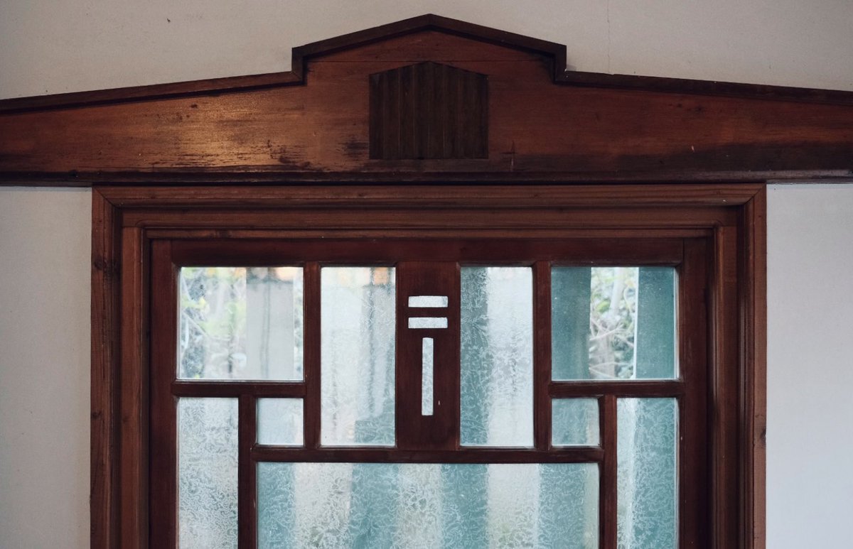 郵便局舎の窓枠詳細。〒マークの透かし彫りが施された格子窓