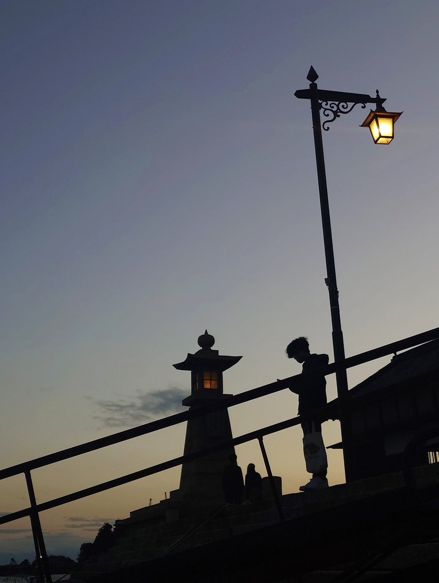 鞆の浦常夜燈の夕暮れシルエット。灯りがともり、港の風景を幻想的に照らす