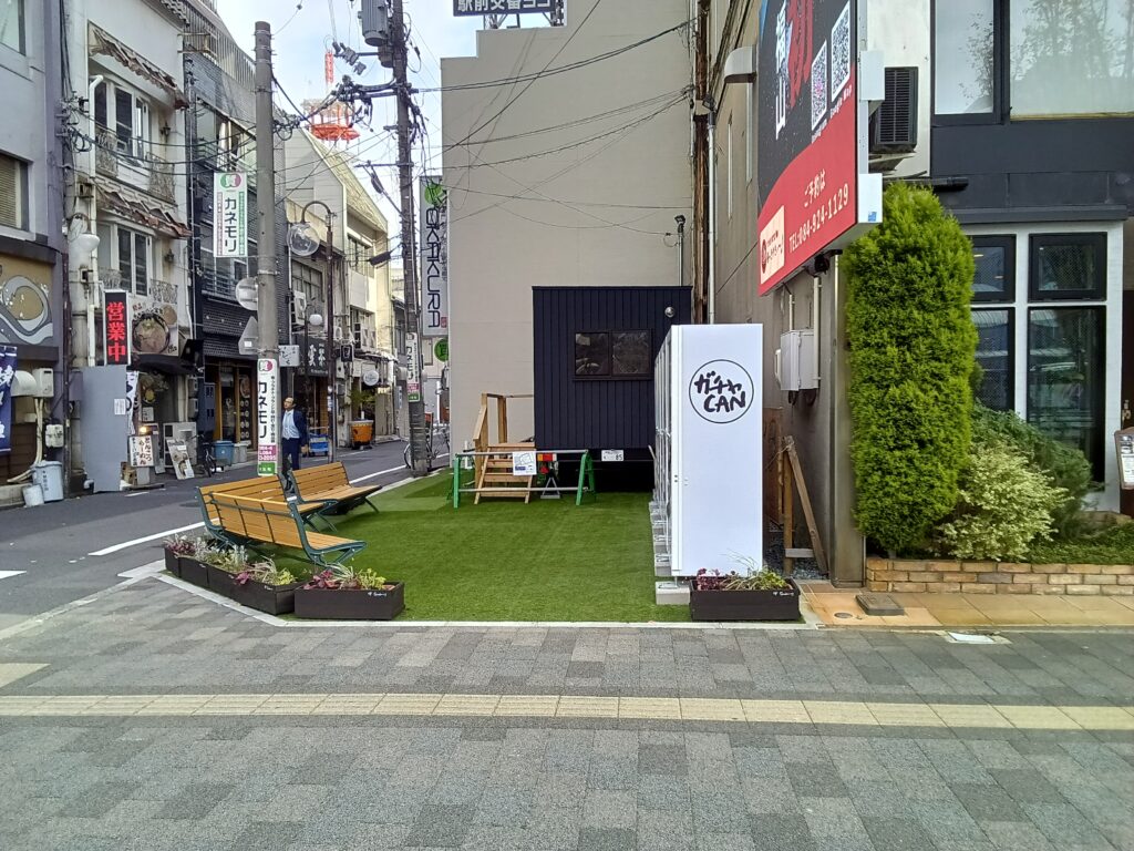 同じ「コウバンアトチ」敷地内のガチャCAN設置状況を、西側から捉えた全景。北側正面とは異なる奥行きで、5台の配置と周辺の歩道との関係がわかる。