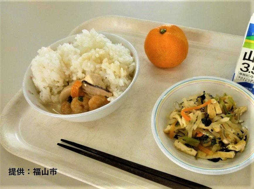 学校給食の食卓をイメージした写真。ご飯、汁物、副菜、果物、牛乳が並ぶ風景