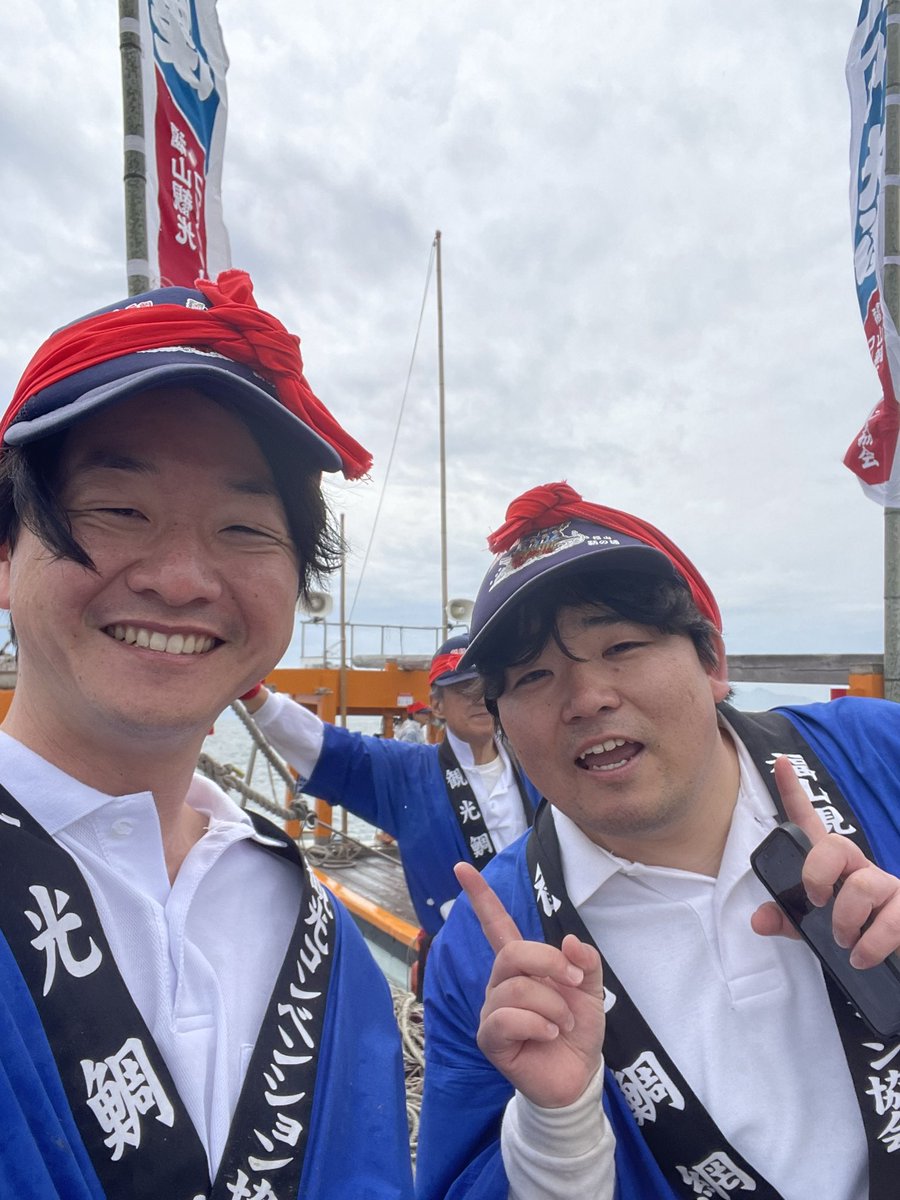地元の参加者と漁師が船上で笑顔を交わす近景のイメージ。顔立ちの特定再現を避け、行事の一体感に焦点を当てる。