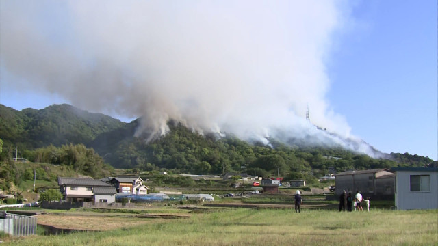 FNNプライムオンライン配信記事に掲載された、福山市赤坂町の山林火災現場の報道写真（ヘリコプターによる消火活動が続く様子）