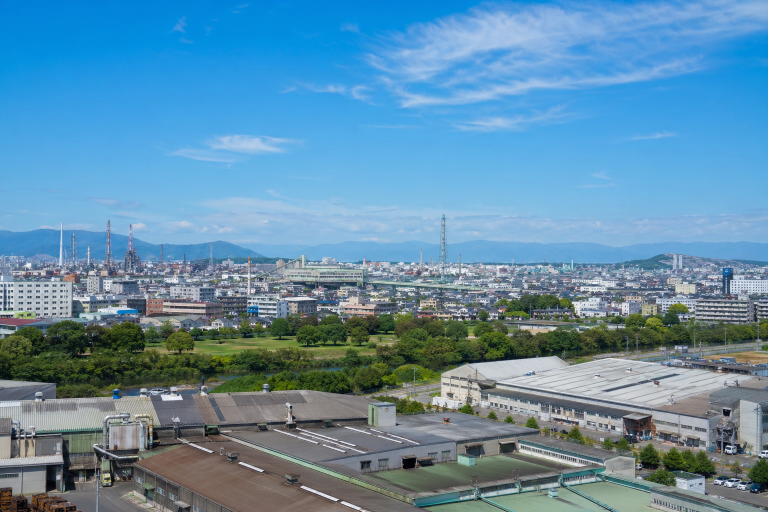 工場屋根と緑地が同居する地方都市の産業風景のイメージ。福山市内の特定施設を示すものではありません。※AIにより生成した参考イメージです。