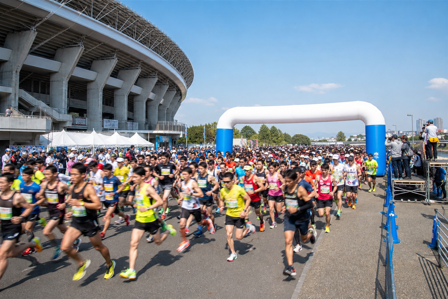 第44回ふくやまマラソンのスタートをイメージした風景。陸上競技場前で多数のランナーが一斉に駆け出し、春の青空と河川敷が広がる開放的な様子（特定個人の再現ではありません）。